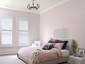 Pink bedroom white ceiling chandelier pink bed cover and pillows with white bedside table and plant